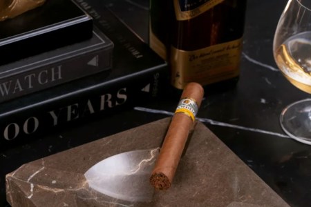a stock shot of a cigar and ashtray, as well as books and whiskey, on a marble countertop