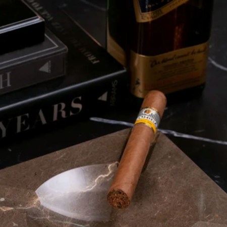 a stock shot of a cigar and ashtray, as well as books and whiskey, on a marble countertop