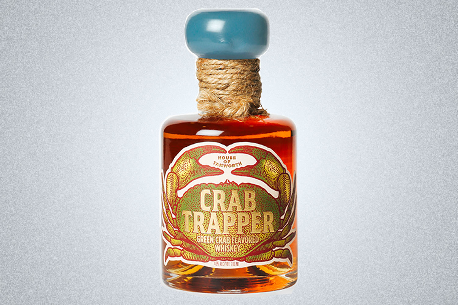 a bottle of amber whiskey called Crab Trapper with a blue cap on a gray background