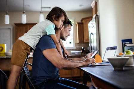 A son leaning on his dad who is typing on a computer. "Dad blogs" have not quite taken off to the level of mom blogs.