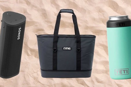 A Sonos Roam speaker, RTIC insulated tote bag and Yeti can insulator, all pictured on a sandy beach background