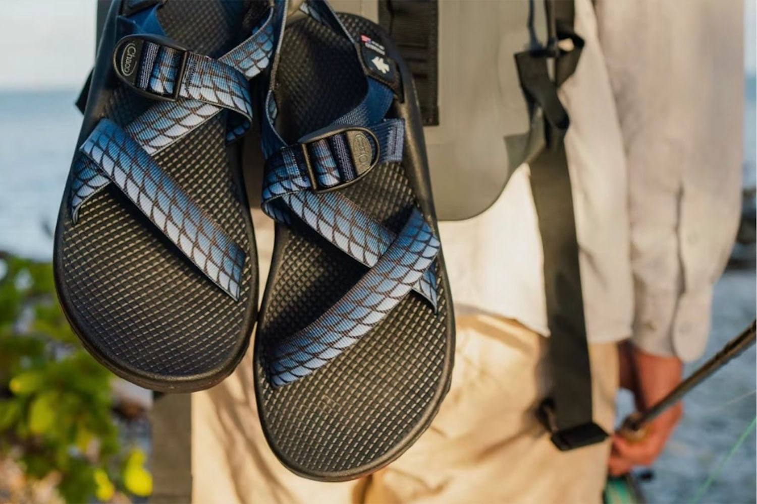 a model shot of the blue strapped, black-soled Huckberry X Chaco Snadals hanging off of a backpack