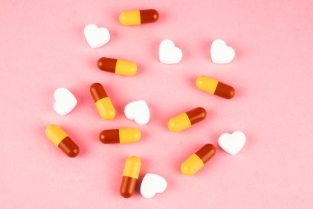 Yellow and red pills and heart-shaped pills scattered on a pink background