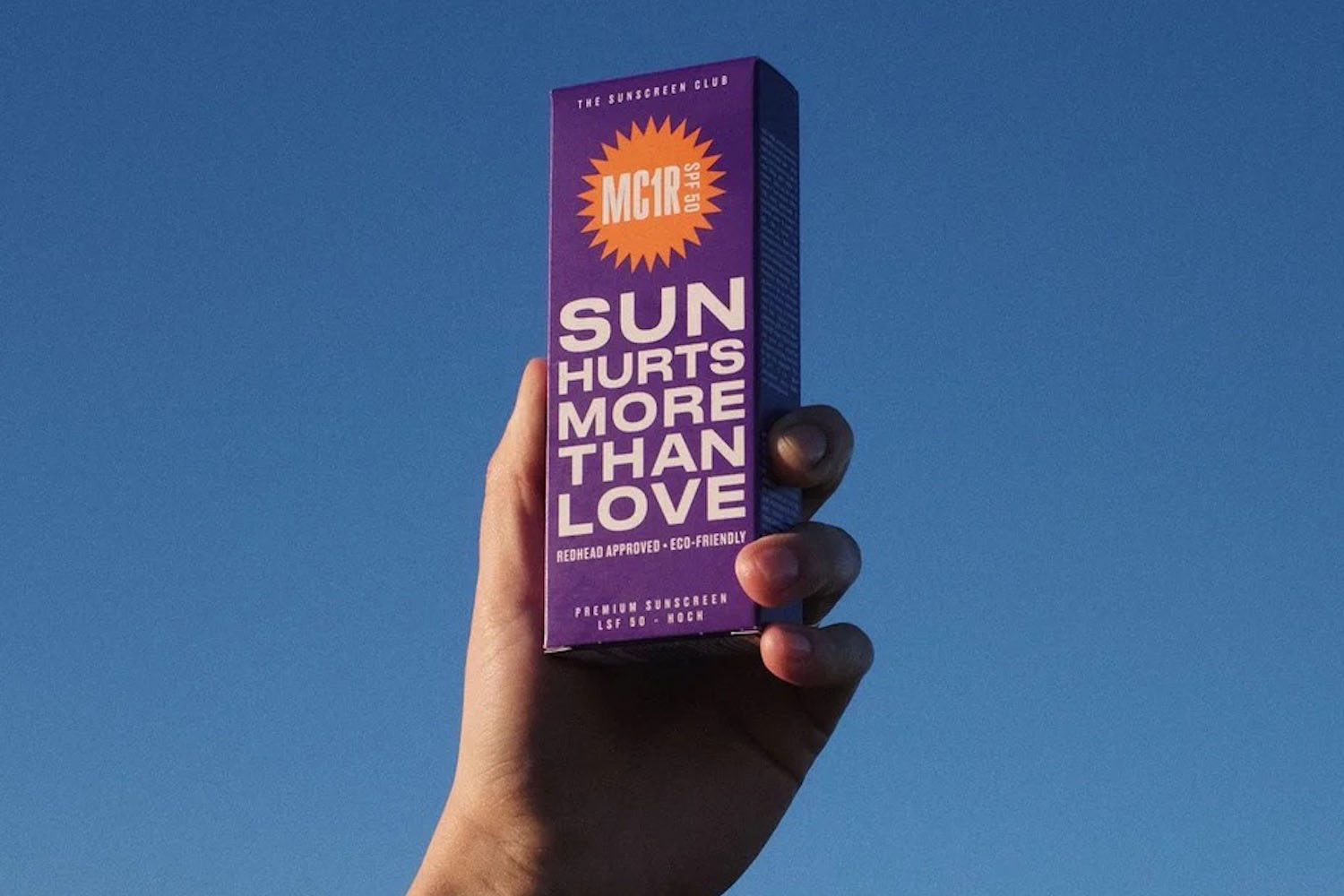 a hand holding a box of MC1R sunscreen against the sky