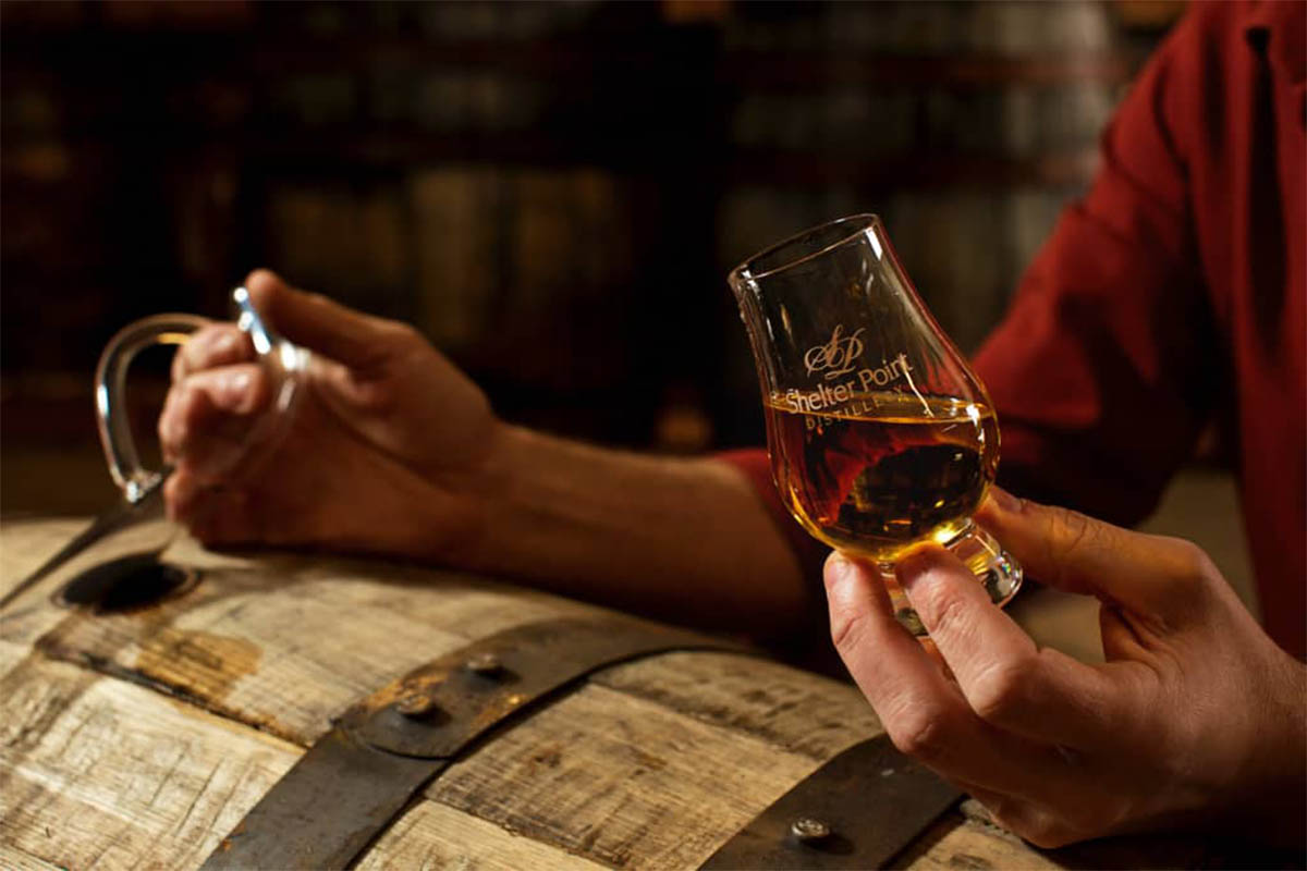 A glass of Shelter Point, a Canadian whisky we recommend, on top of a barrel being held in a hand