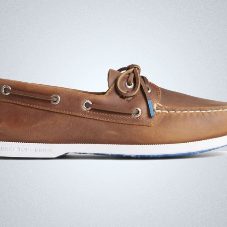 a pair of brown leather, white-soled and blue detailed boat shoes from Sperry on a grey background