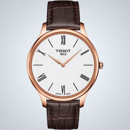 a brown-leather strapped, gold-rimmed, white faced watch with gold detailing and roman numerals from Tissot on a grey background