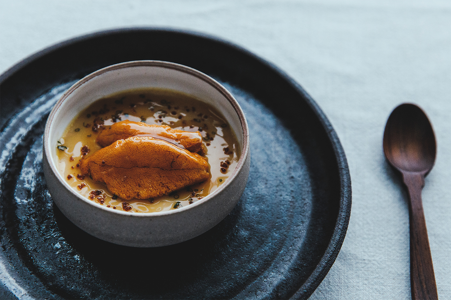 The purple sea urchin dish Uni Chawanmushi plated with a spoon next to it on a table at at Harbor House Inn in Mendocino