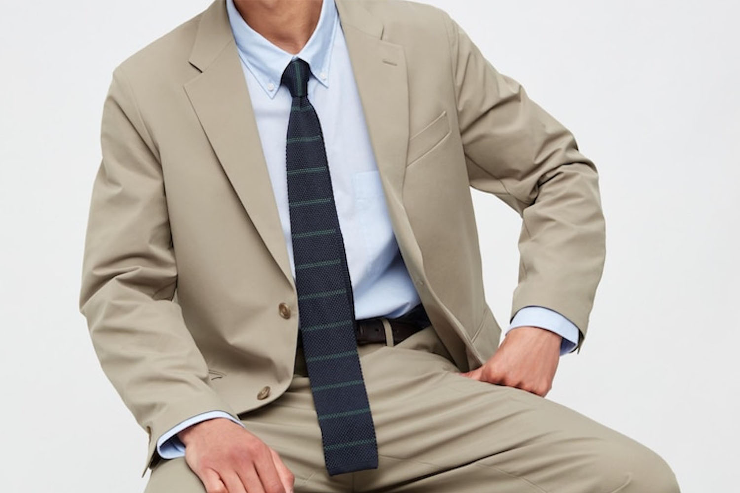 a model in a biege uniqlo suit, blue shirt and blue tie, sitting down