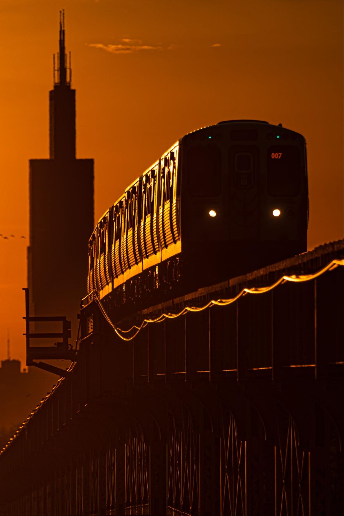 A train from Chicago's L line riding across the tracks at sunrise with the Willis Tower (formerly the Sears Tower) in the background