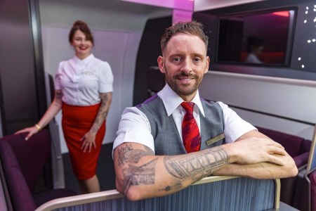 Virgin Atlantic flight attendants with tattoos, a man with his arms crossed up front and a woman standing in the back. Virgin just announced it will allow attendants to display certain tattoos.