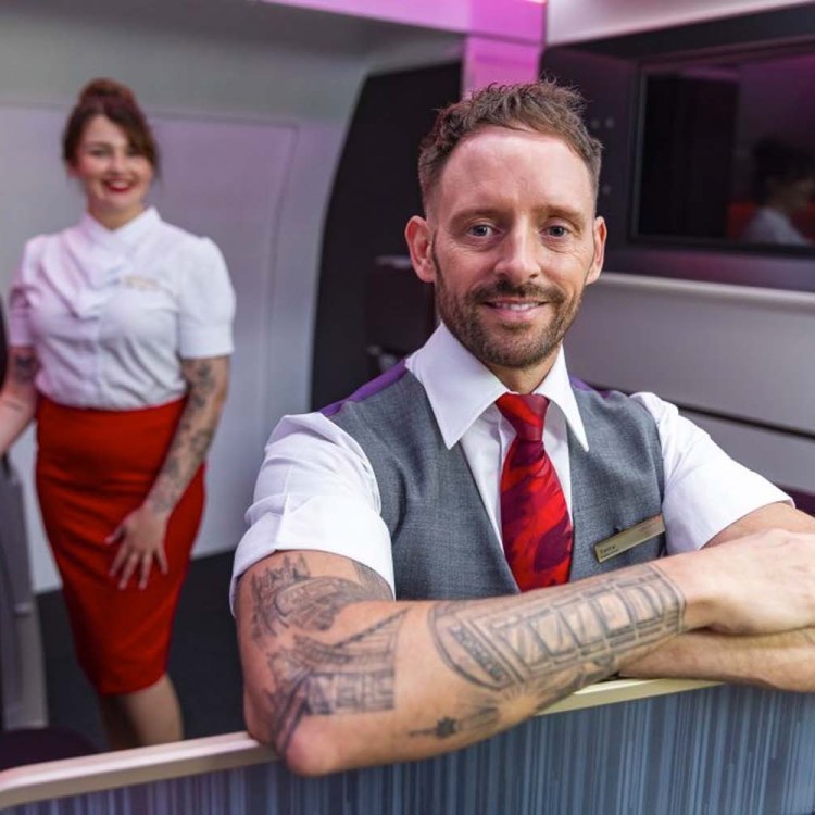 Virgin Atlantic flight attendants with tattoos, a man with his arms crossed up front and a woman standing in the back. Virgin just announced it will allow attendants to display certain tattoos.