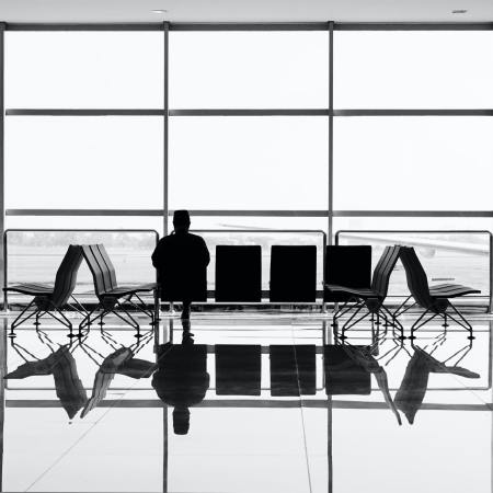 A black and white photo of a person sitting alone in an airport terminal looking out the window