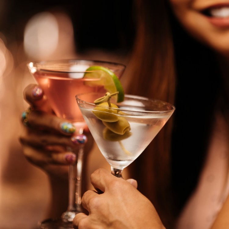 Close-up photo shows a couple clinking martini glasses on a date at a bar