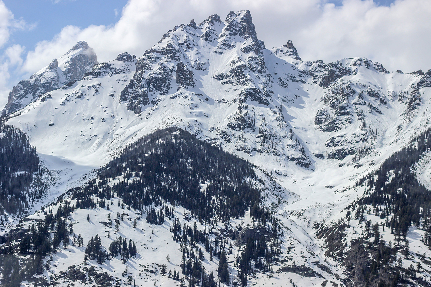 A snow-capped mountain peak of the Teton mountain range with a blue sky and white clouds above