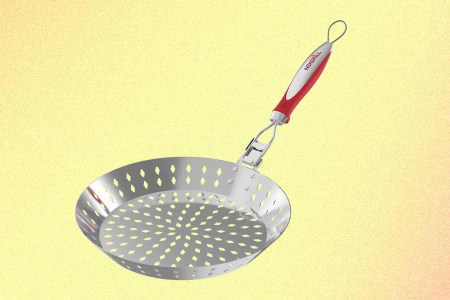 A grilling skillet from Nexgrill with a red handle and holes in the stainless steel basket, pictured on a yellow background.