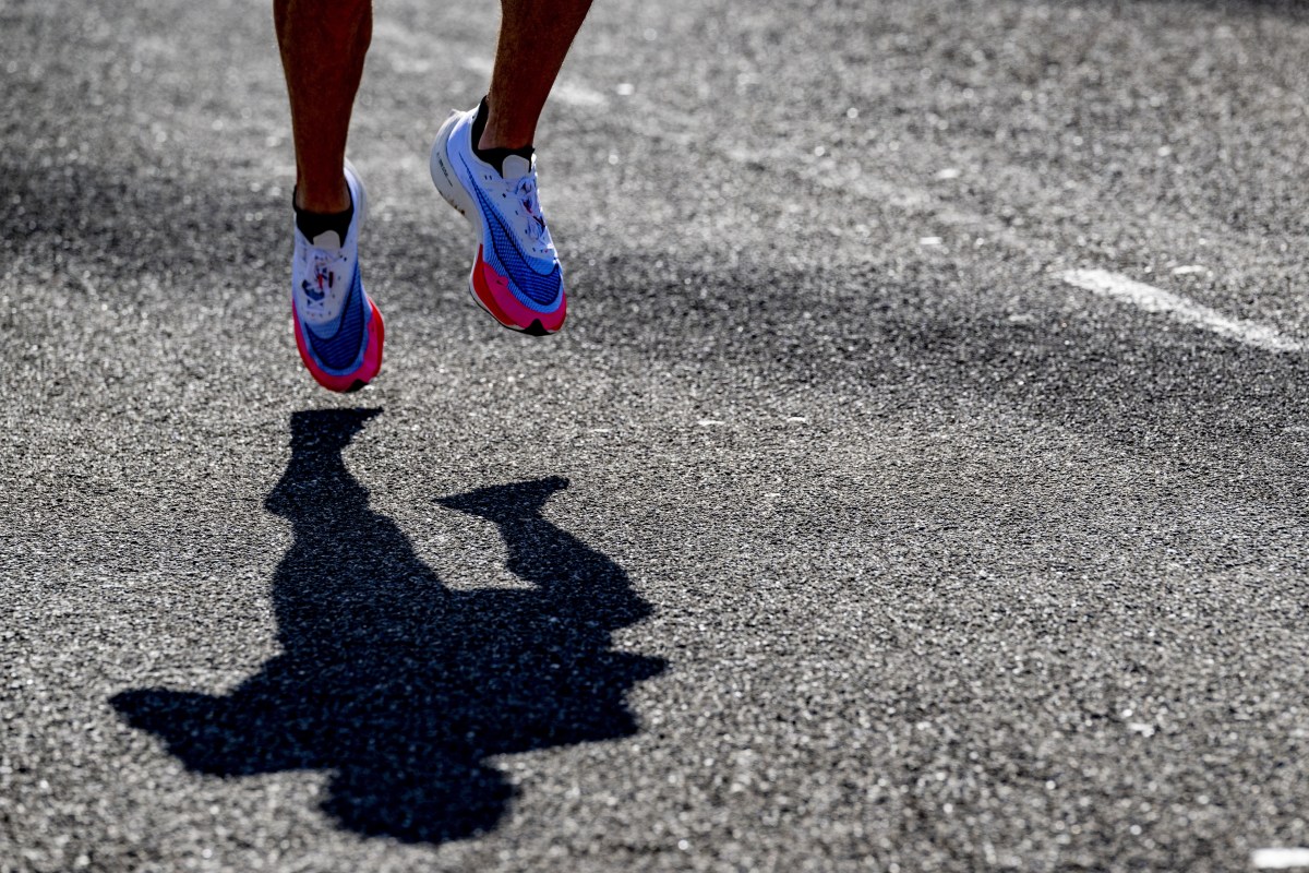 A view of two Nike running sneakers on black pavement, over a shadow of a runner.