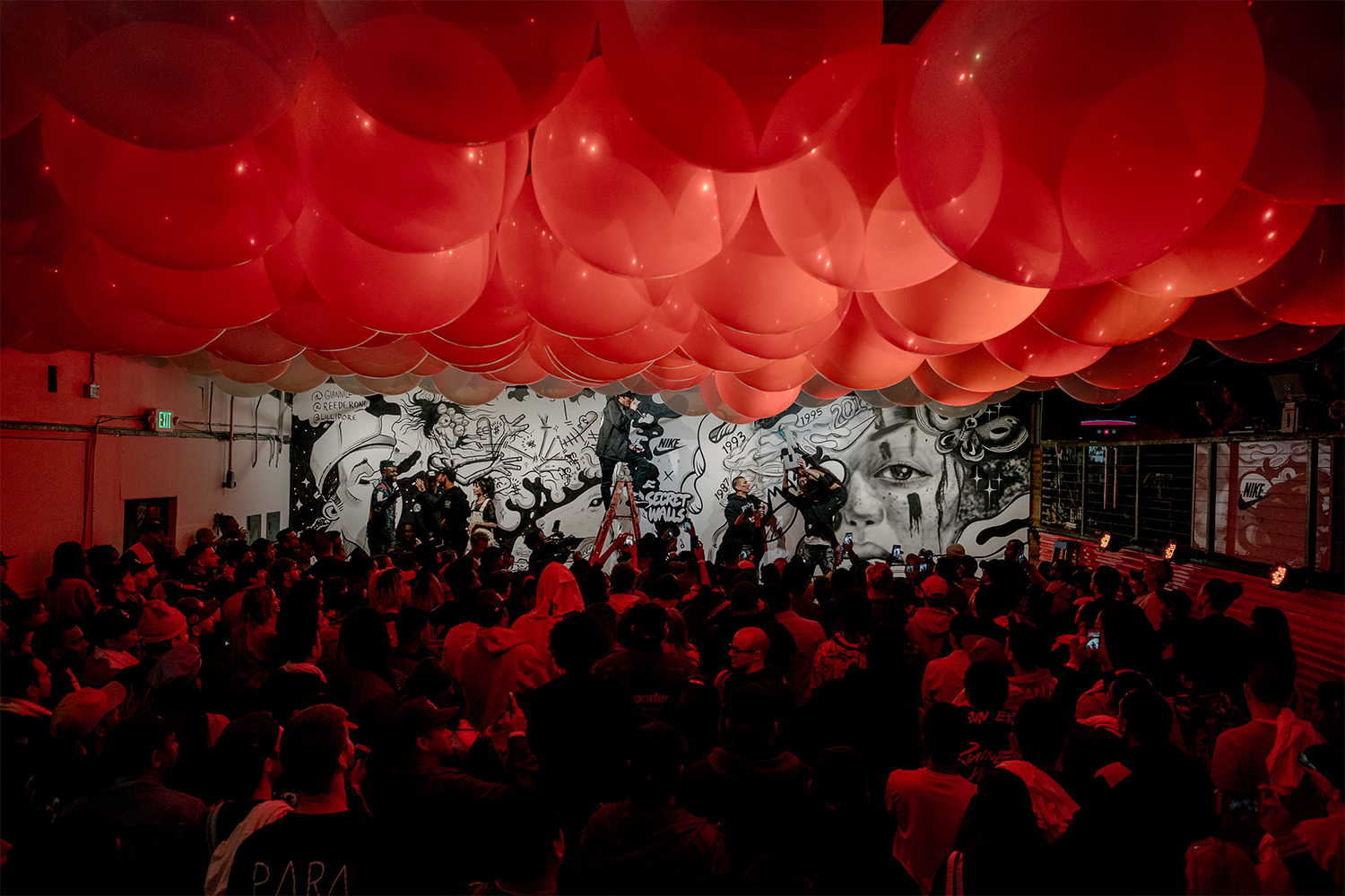 A ceiling covered in balloons over a crowd of people at a Secret Walls event where two artists face of in painting black and white murals
