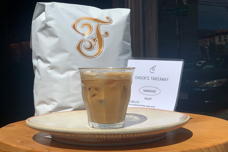 A Vietnamese coffee from Chuck's Takeaway in San Francisco sits on a plate next to a bag of Saint Frank coffee beans