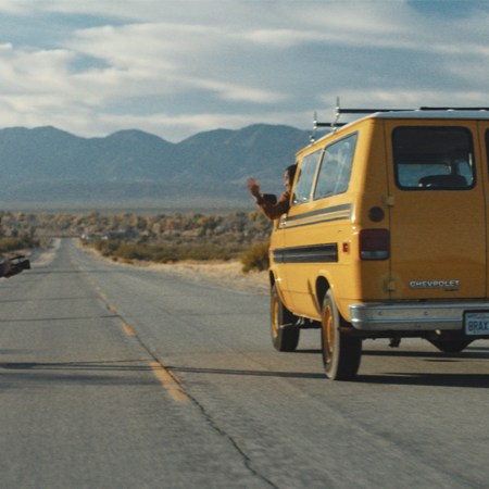 Man skateboards beside a moving yellow van on empty highway