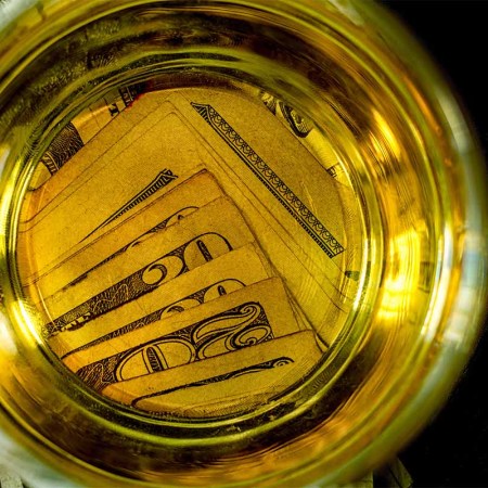 A glass of alcohol on top of twenty dollar bills.