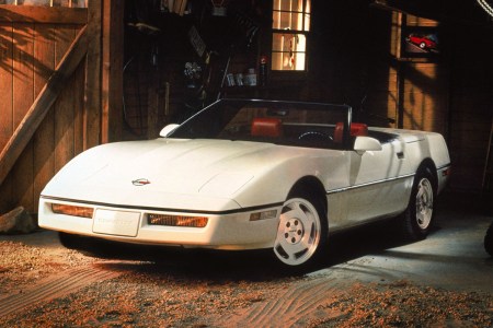 A white Chevrolet Corvette C4 convertible in a garage with light shining on the hood