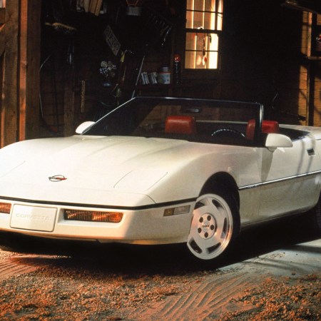 A white Chevrolet Corvette C4 convertible in a garage with light shining on the hood