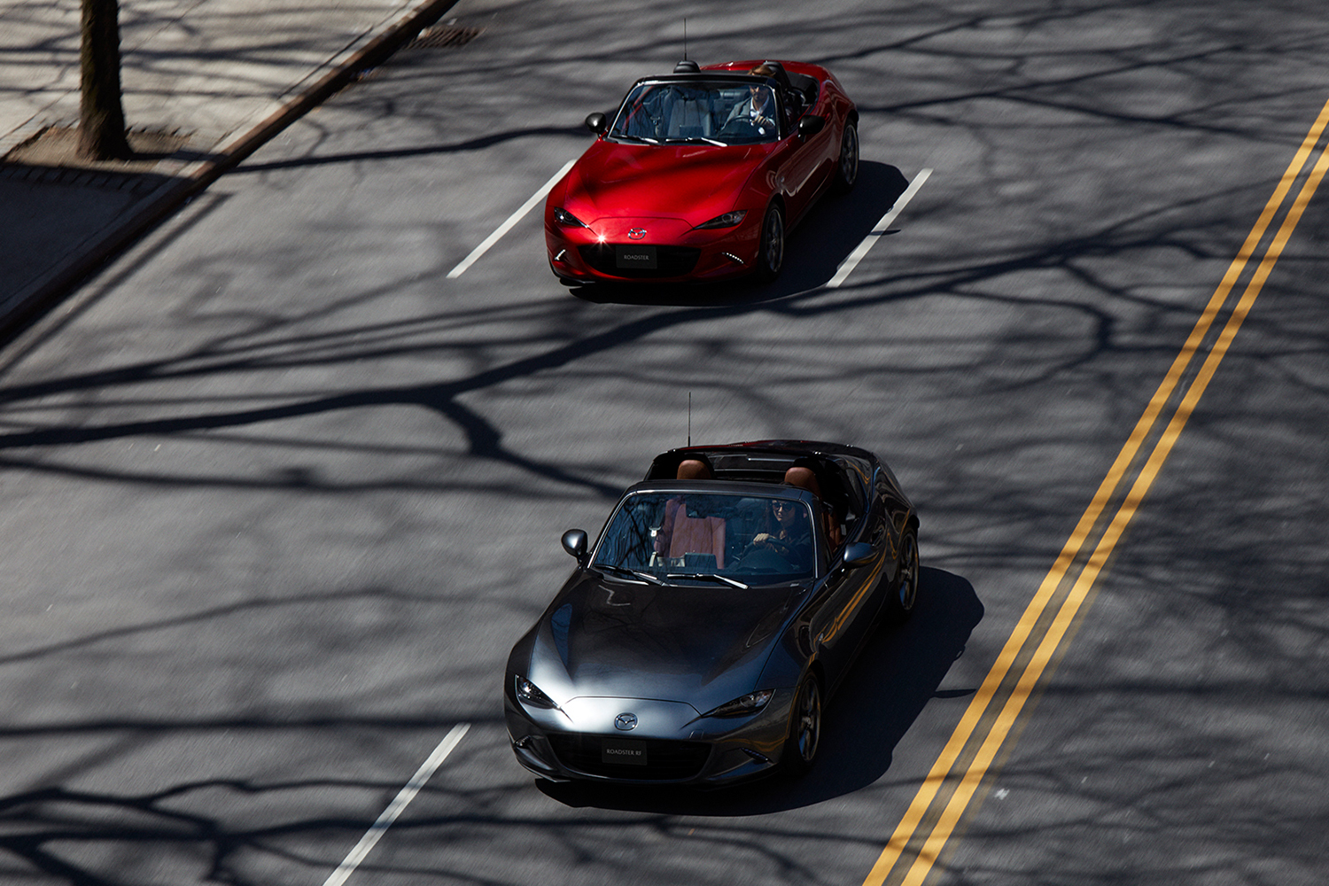 Two 2022 Mazda MX-5 Miata convertibles photographed from overhead driving down a city street