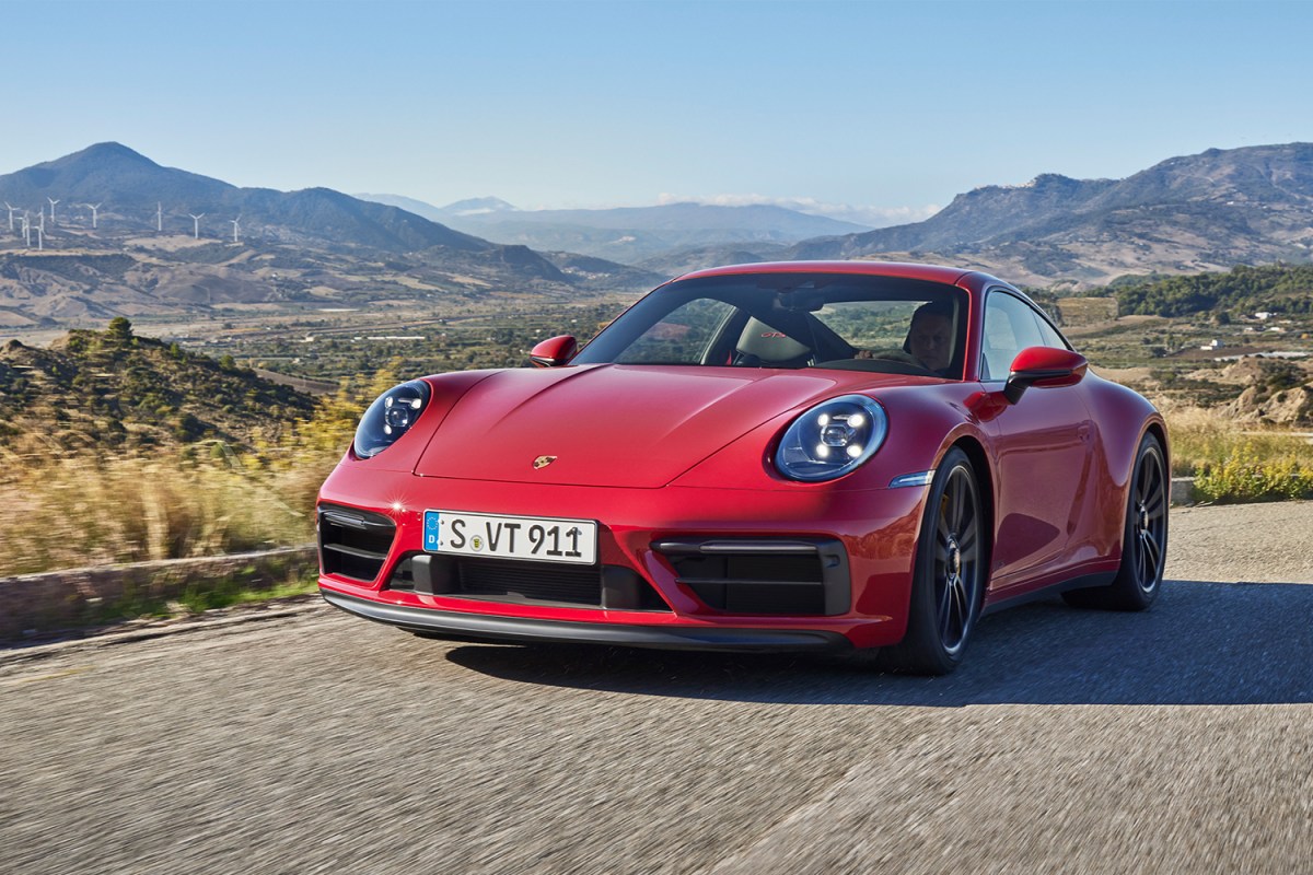 A red 2022 Porsche 911 Carrera GTS driving down a rural road with windmills and hills in the background