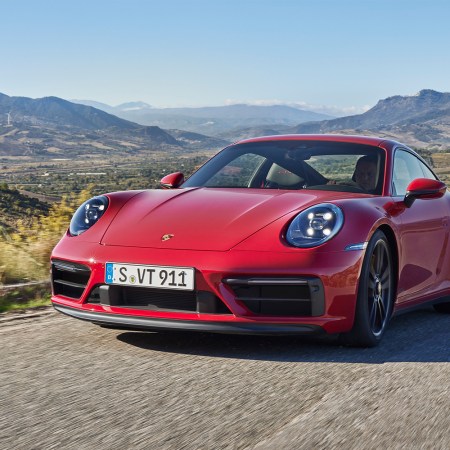 A red 2022 Porsche 911 Carrera GTS driving down a rural road with windmills and hills in the background