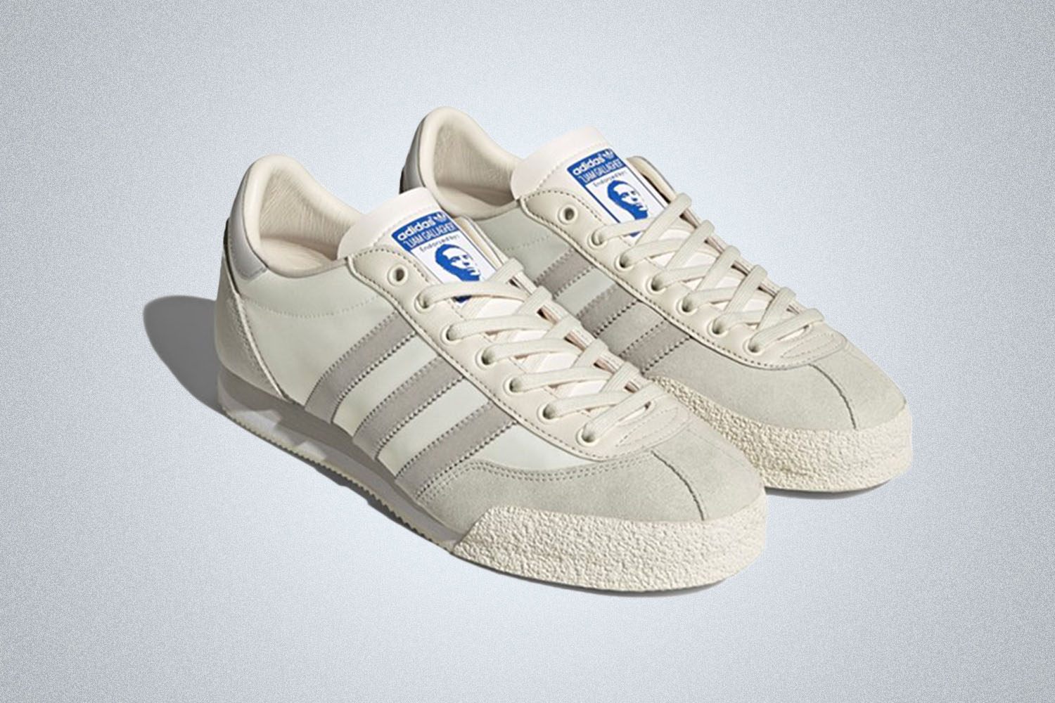 a pair of white adidas trainers in collaboration with Liam Gallagher on a grey background