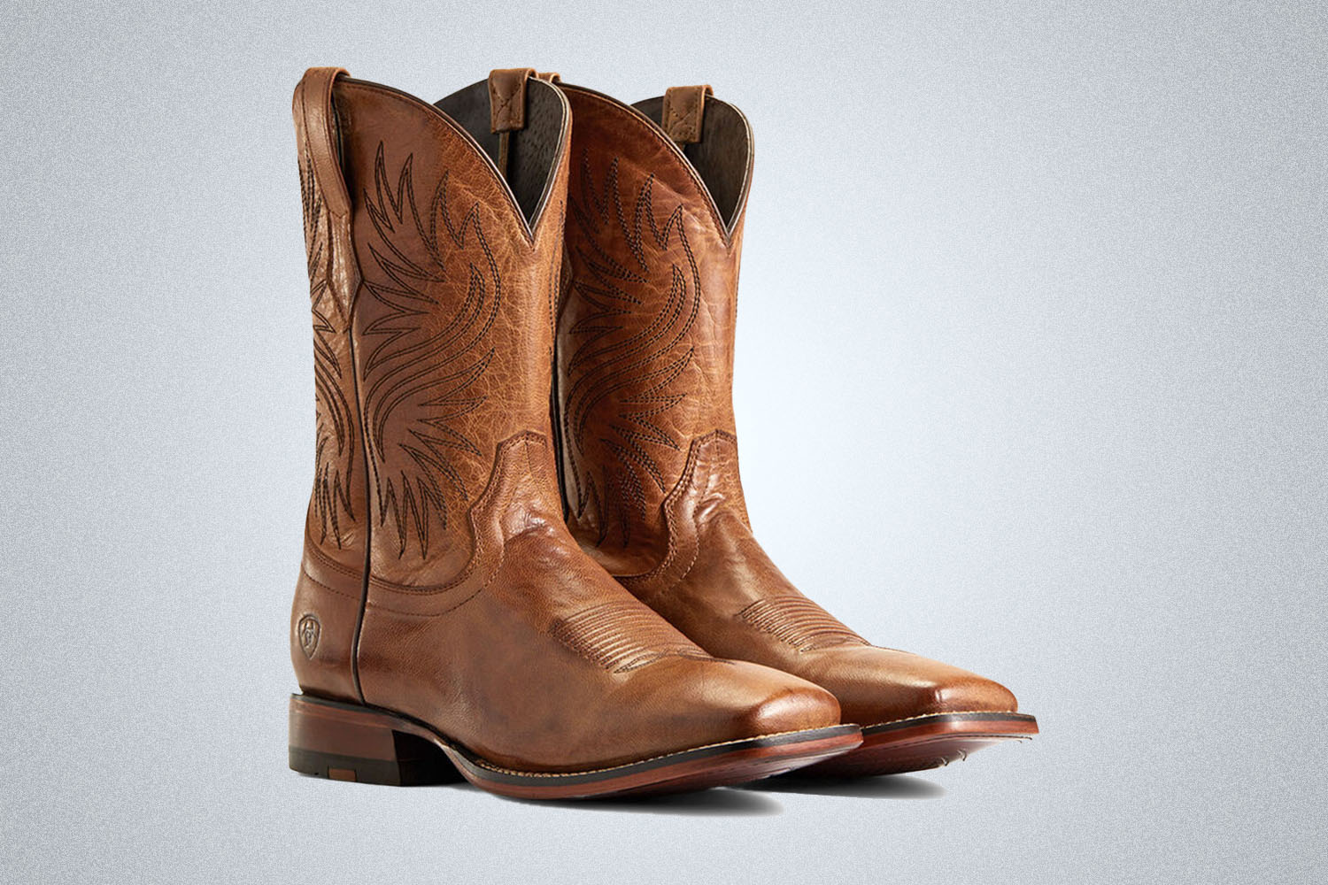 a pair of brown cowboy boots from Ariat on a grey background