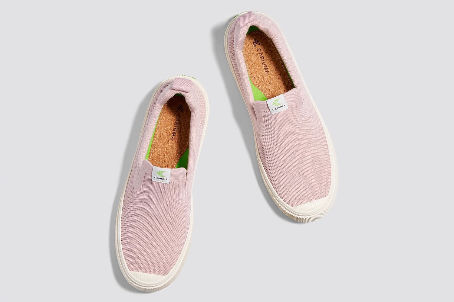 a pair of pink Cariuma slip on sneakers on a grey background