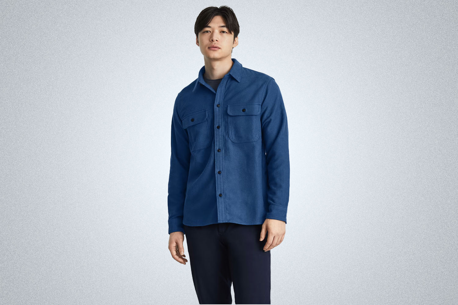 a model in a woven navy blue overshirt from Everlane on a grey background