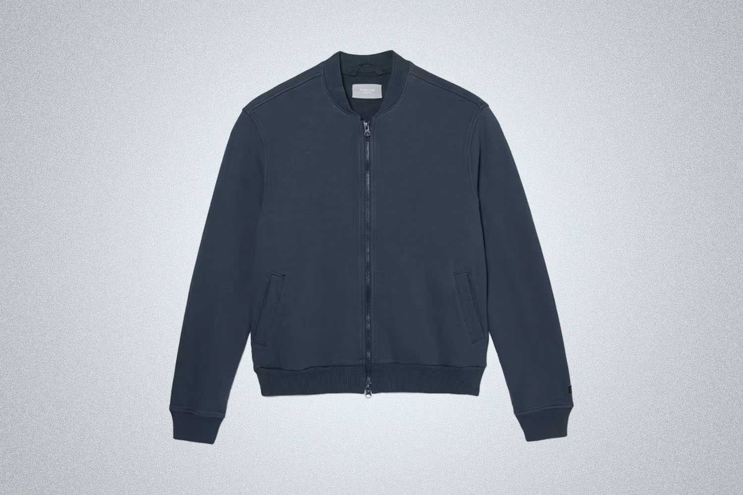 a blue knit track bomber jacket from Everlane on a grey background