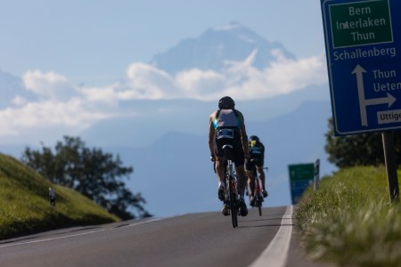 A man biking on a road in Switzerland with a mountain and clouds in the background