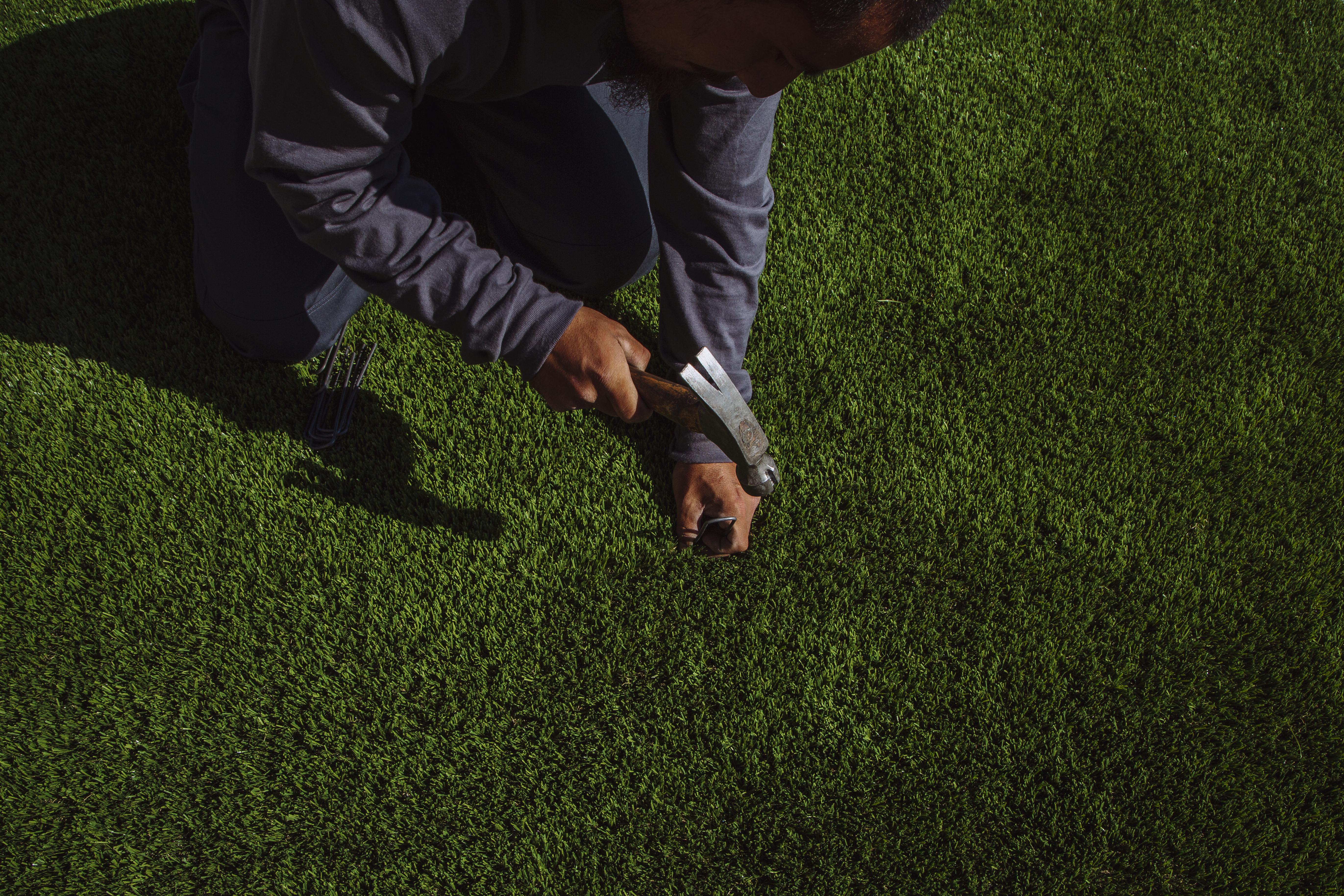 A man nails artificial turf down over a lawn. Here's why green synthetic lawns are catching on.