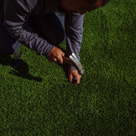 A man nails artificial turf down over a lawn. Here's why green synthetic lawns are catching on.