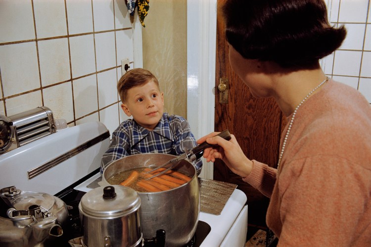 A kid watching his mom boil hot dogs.