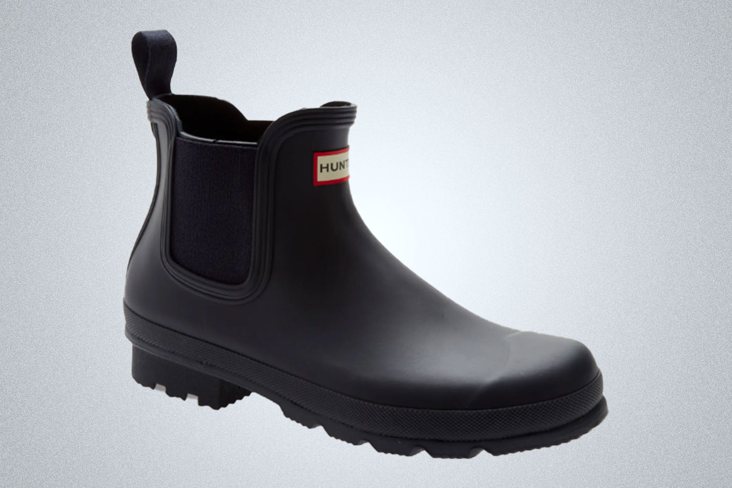 a black lugged rain boot from Hunter on a grey background