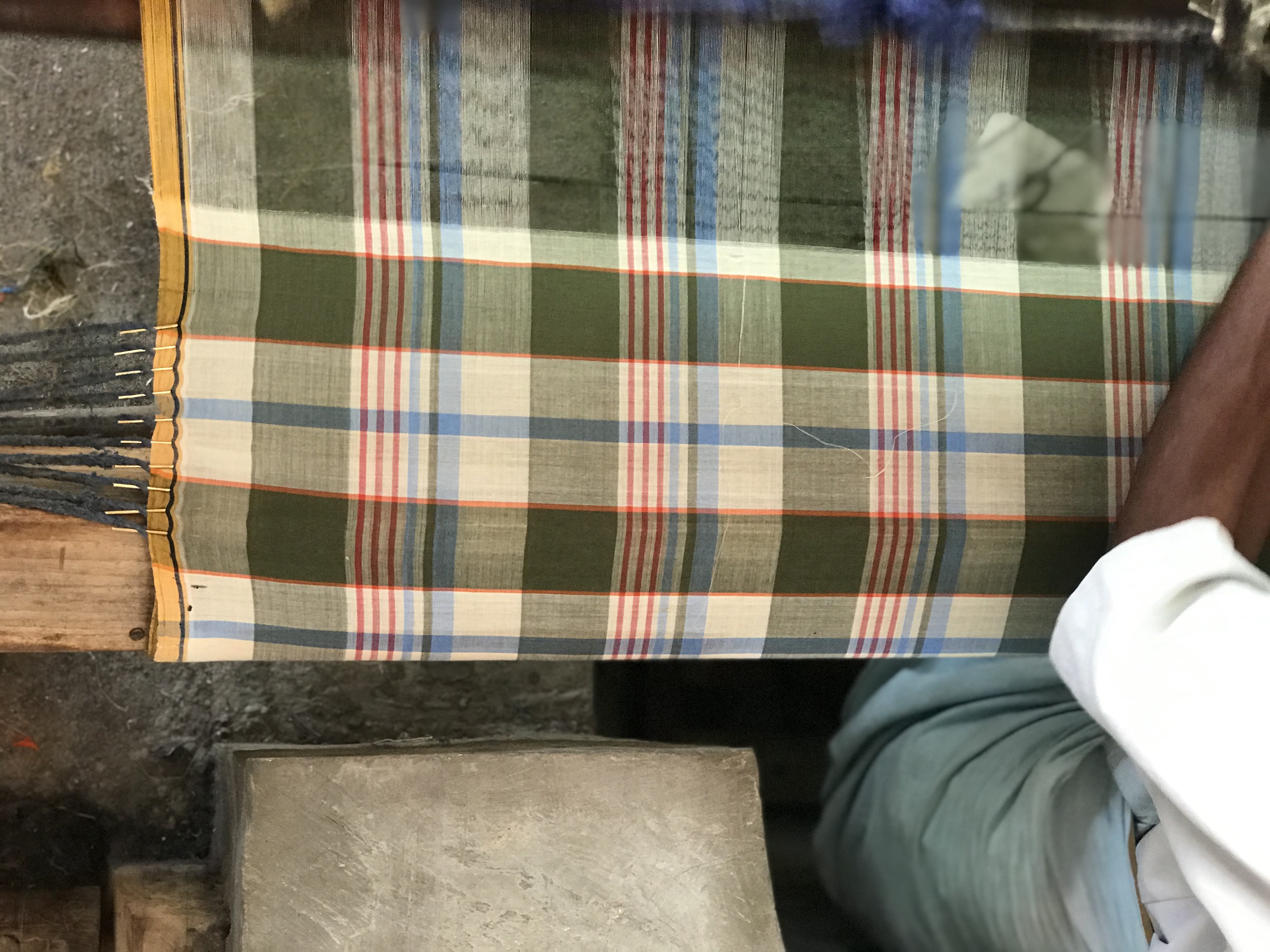 A green, red and beige madras pattern being made by an artisan