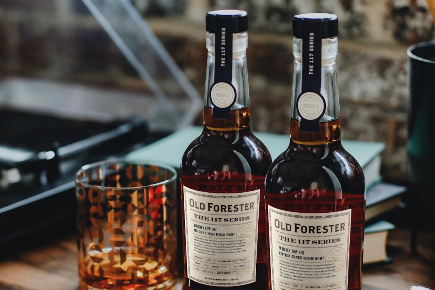 a model shot of two bottles of Old Forester Whiskey and a glass on a table