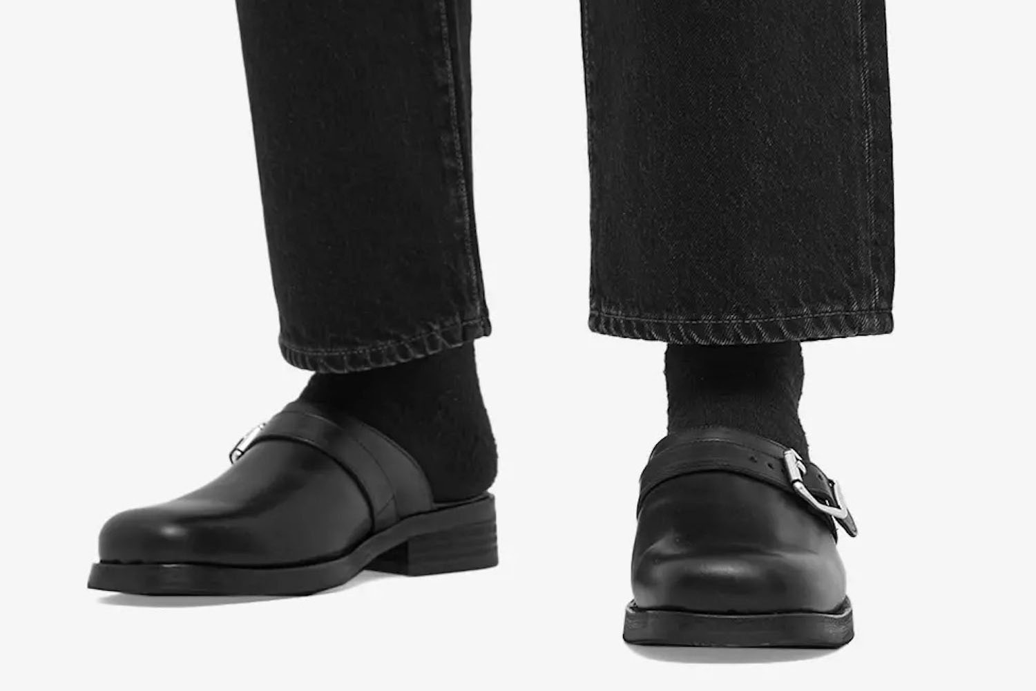 a model wearing the Our Legacy Camion Mules with black jeans and socks on a white background