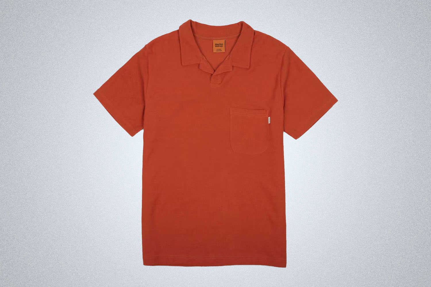 A terracotta red terry polo from Rhythm on a grey background