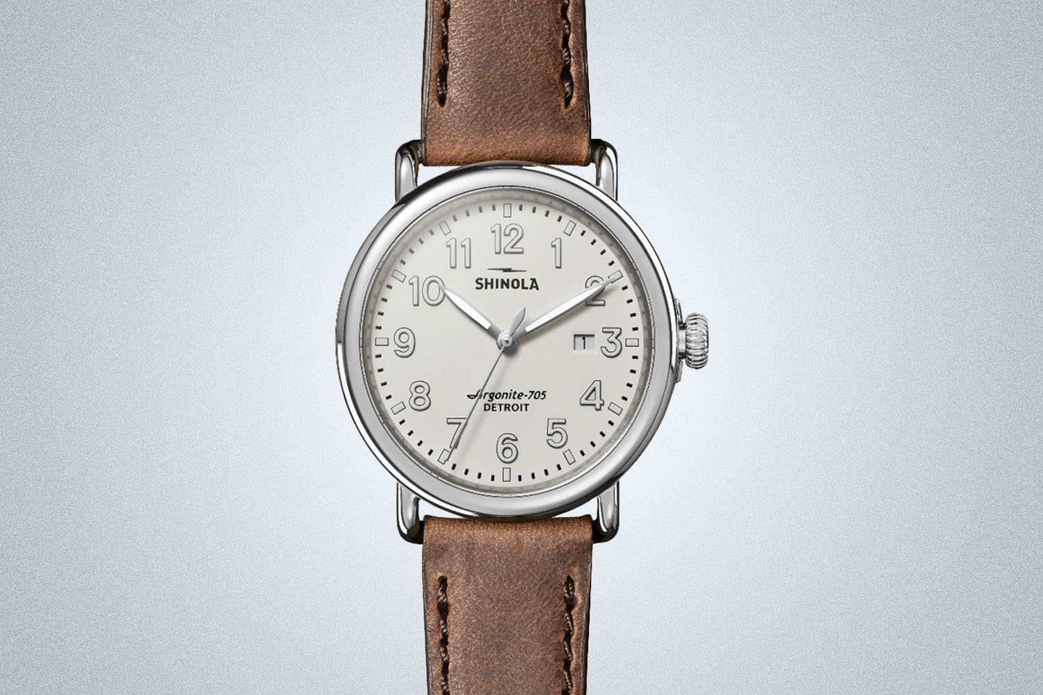 a borwn-leather strapped, silver watch from Shinola on a grey background