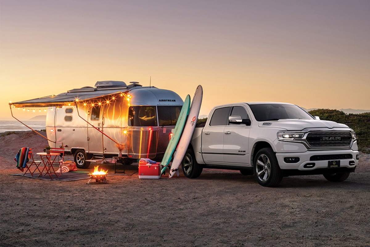 An Caravel 20FB travel trailer from Airstream sits on a beach with string lights behind a Ram 1500 Limited truck. Here's how to win both from Omaze.