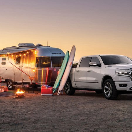 An Caravel 20FB travel trailer from Airstream sits on a beach with string lights behind a Ram 1500 Limited truck. Here's how to win both from Omaze.