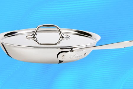 A stainless steel fry pan from All-Clad with a lid on a blue background