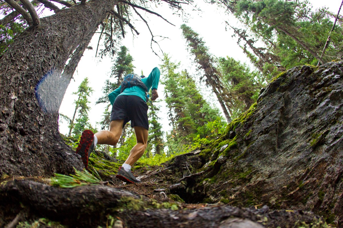 A man runs through lush green woods in trail running gear.