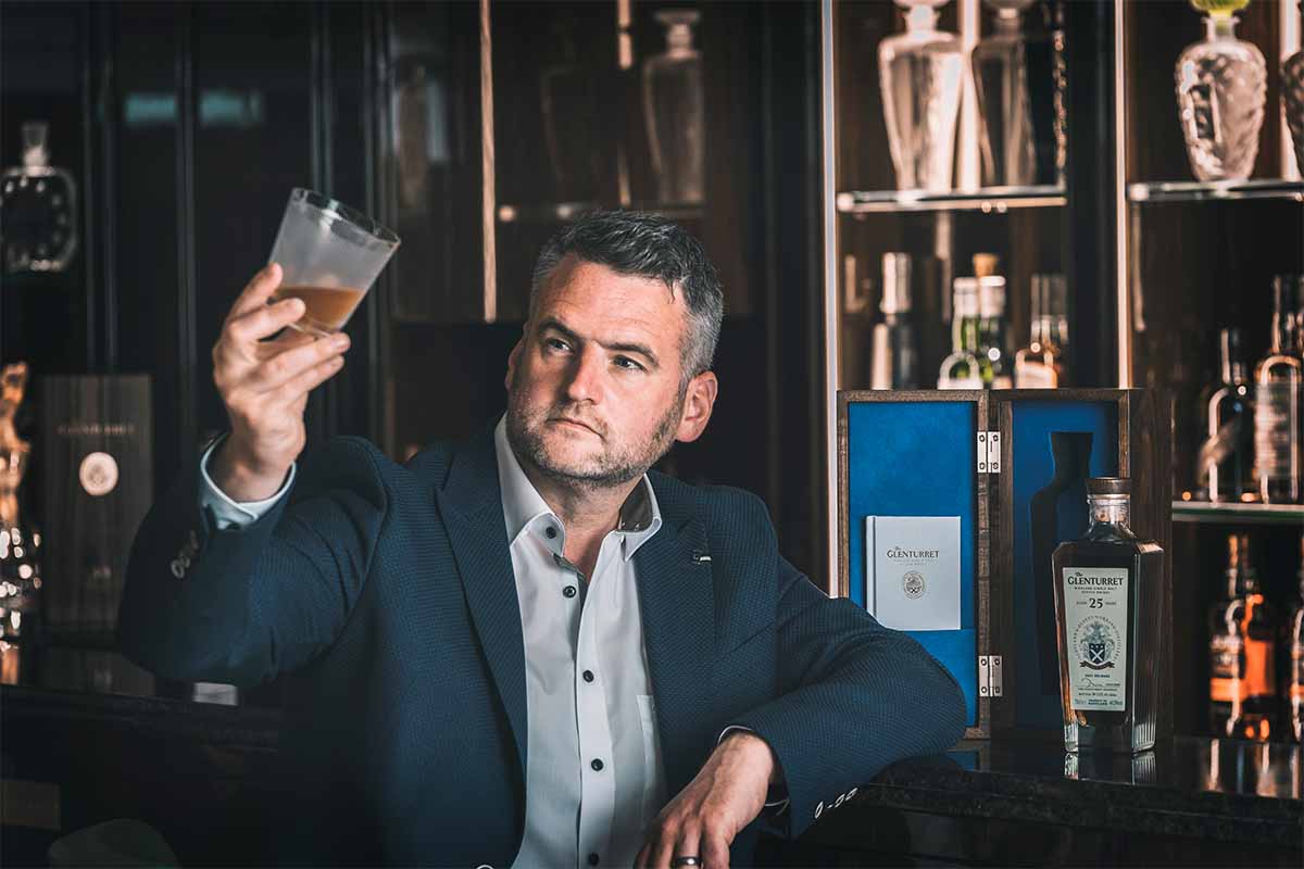 The Glenturret Managing Director John Laurie holding a glass of whiskey at a bar